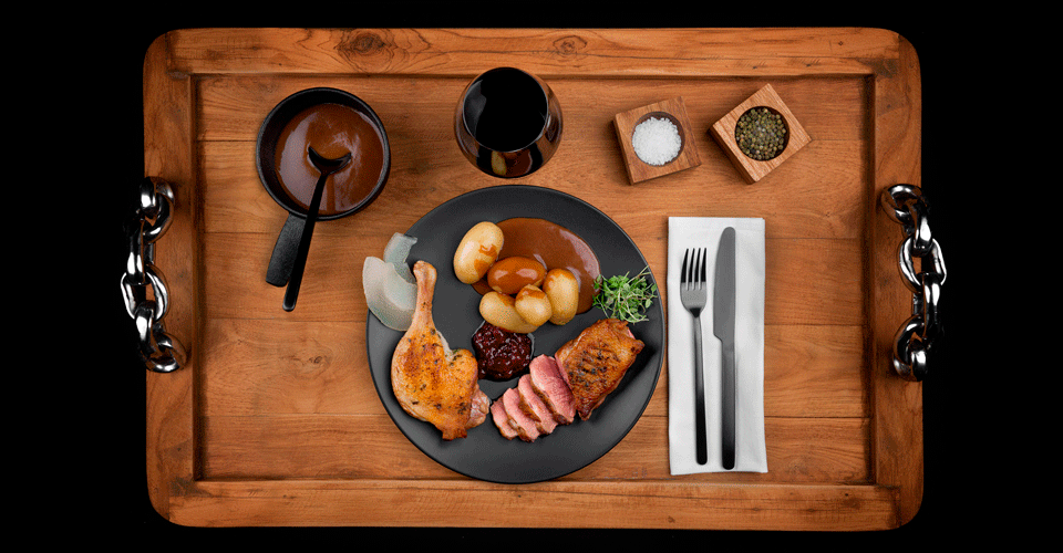 Photo of a dish containing duck, presented on a wooden tray.